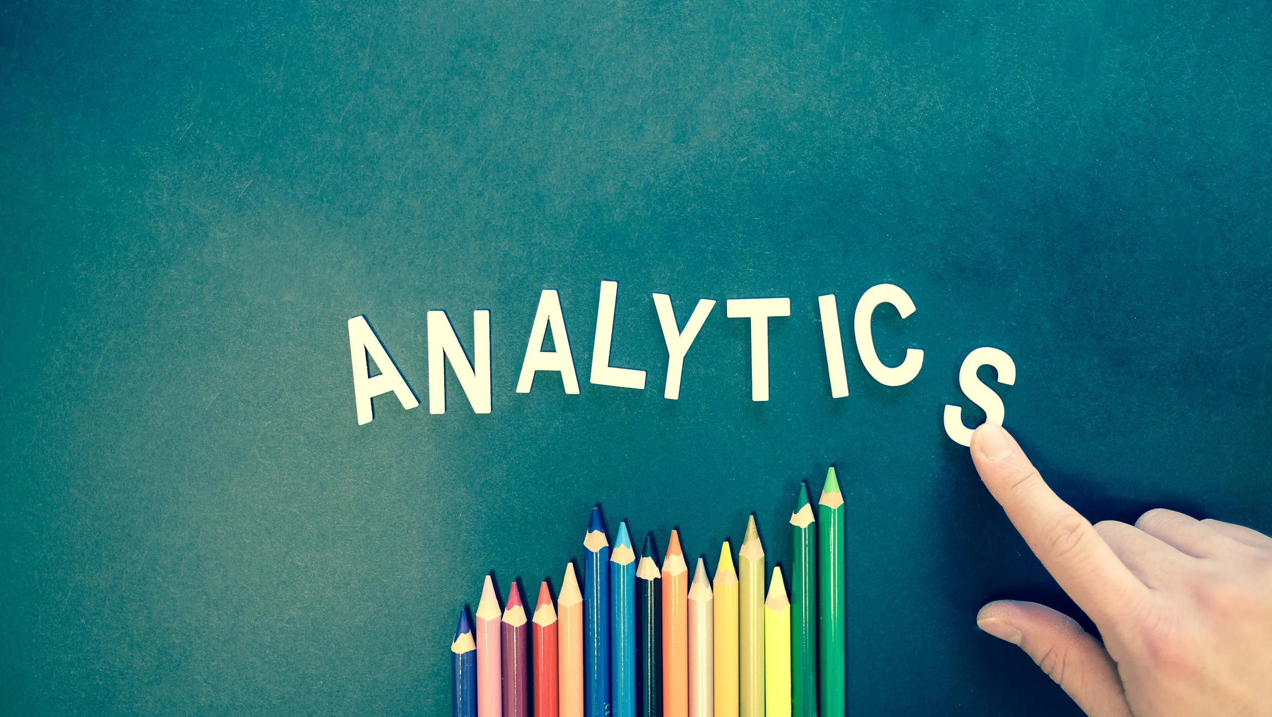 The word 'ANALYTICS' spelled out in white letters with colored pencils below, symbolizing the importance of search engine optimization and data analysis for an AI blog writer to make a blog post noticed.