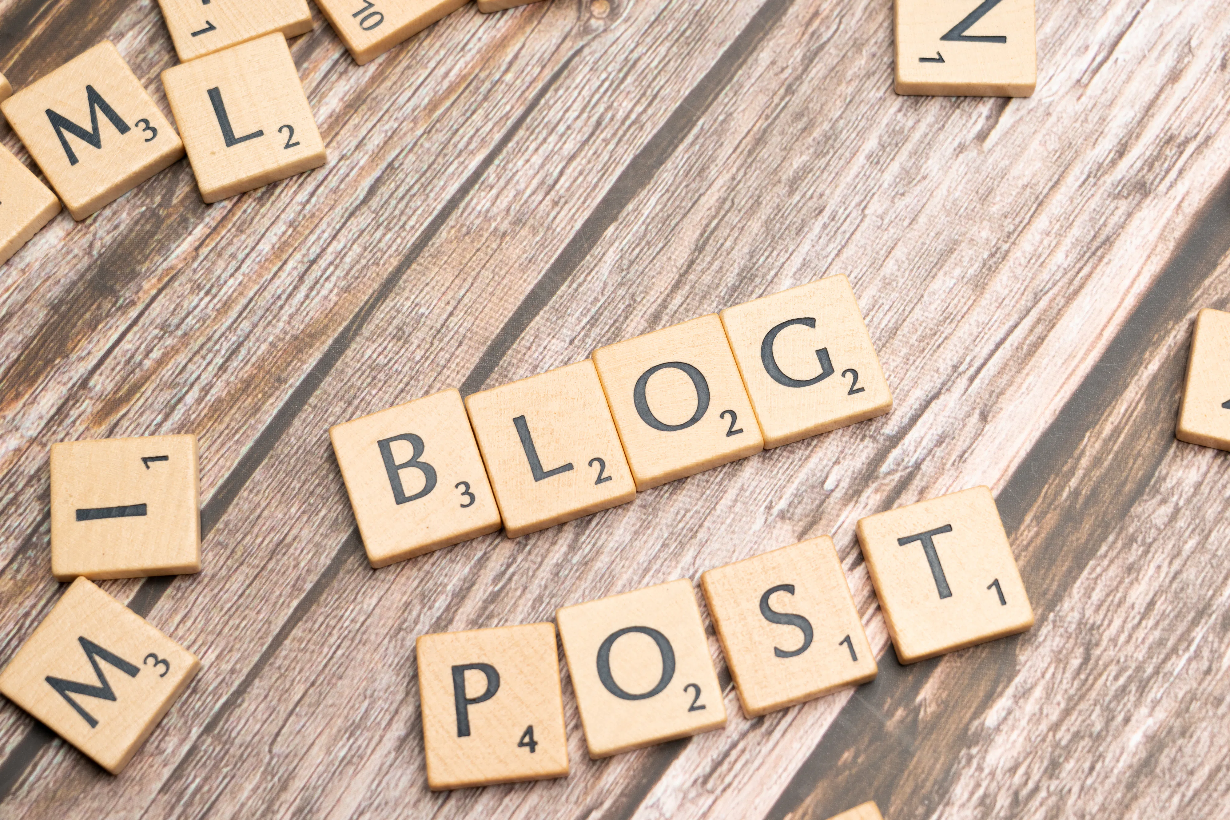 Scrabble tiles spelling out 'BLOG POST' on a wooden surface, symbolizing the essential content of a blog, which AI writing assistance aims to enhance for better search engine optimization and blog post visibility in 2025.