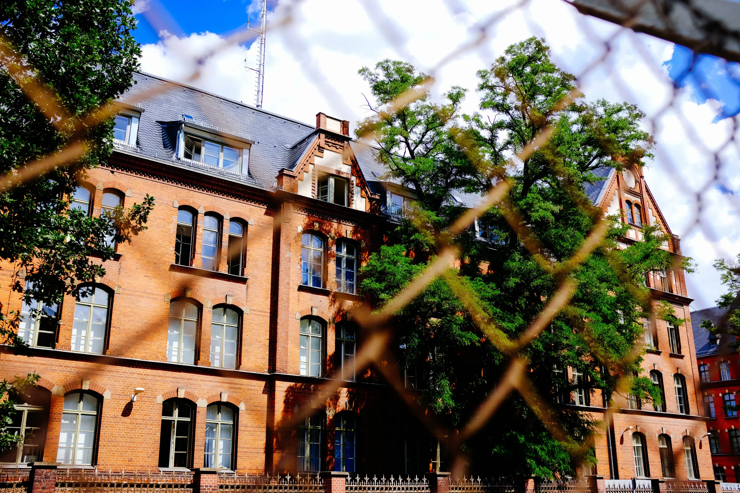 A large, historic brick building with trees in front, viewed through a fence, unrelated to the keywords provided.