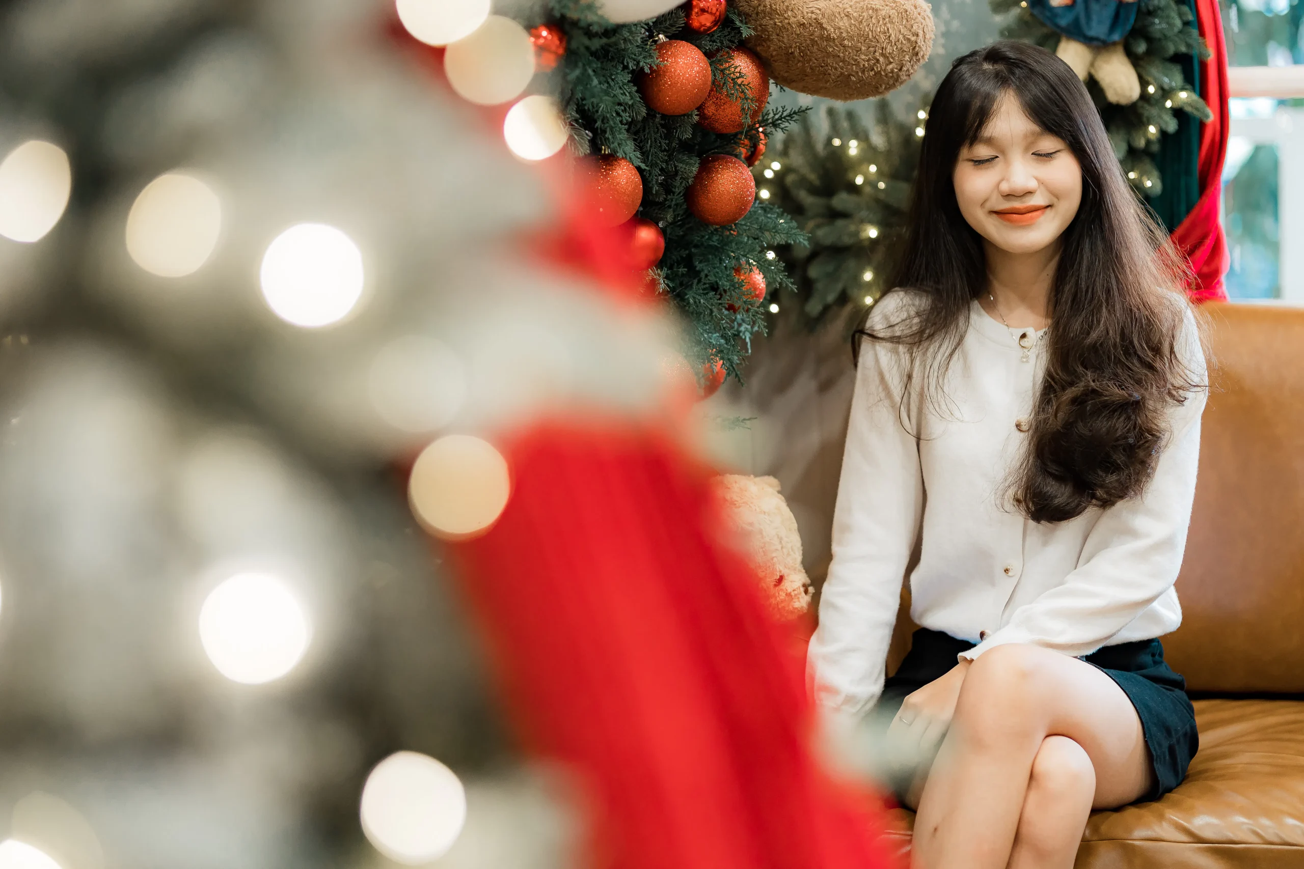 A young woman sitting in front of a decorated Christmas tree, symbolizing the joy of content creation and the festive spirit of planning a successful 2025 content strategy with the help of an AI content creator.