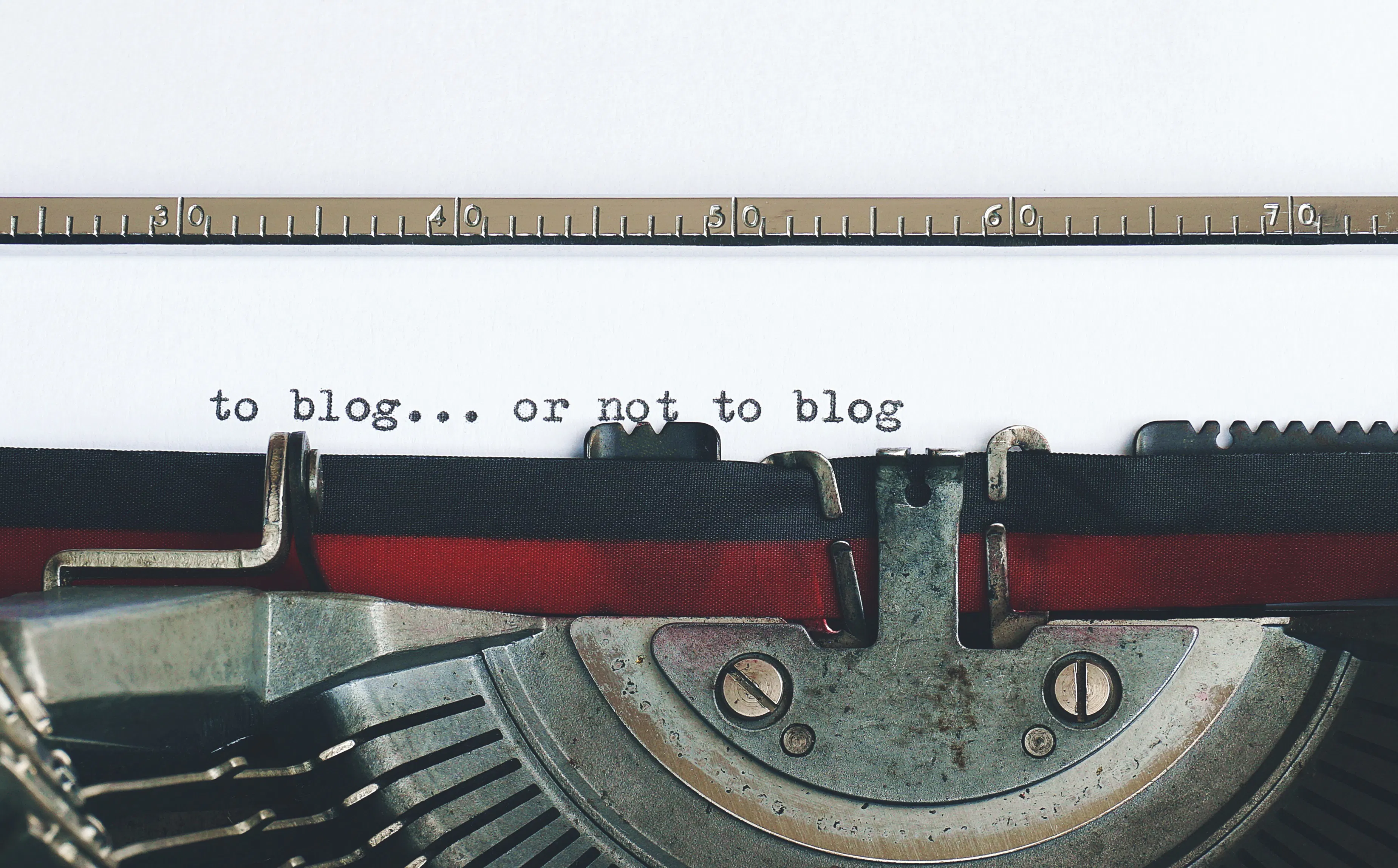 A vintage typewriter with the words 'to blog... or not to blog' typed on a piece of paper, capturing the essential question for anyone considering using a blogging tool or an AI blog writer to increase blog traffic.
