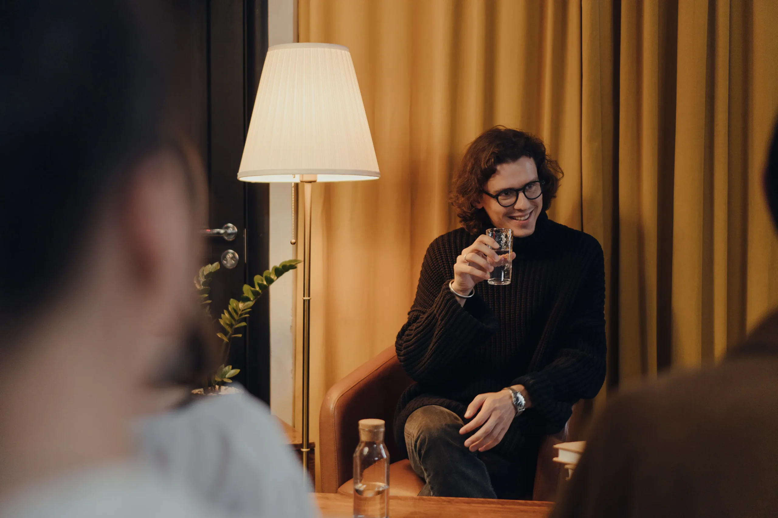 A man in glasses smiles while holding a glass of water in a warm, inviting room, representing the engaging content and personal touch that AI for bloggers aims to enhance in blog post visibility.