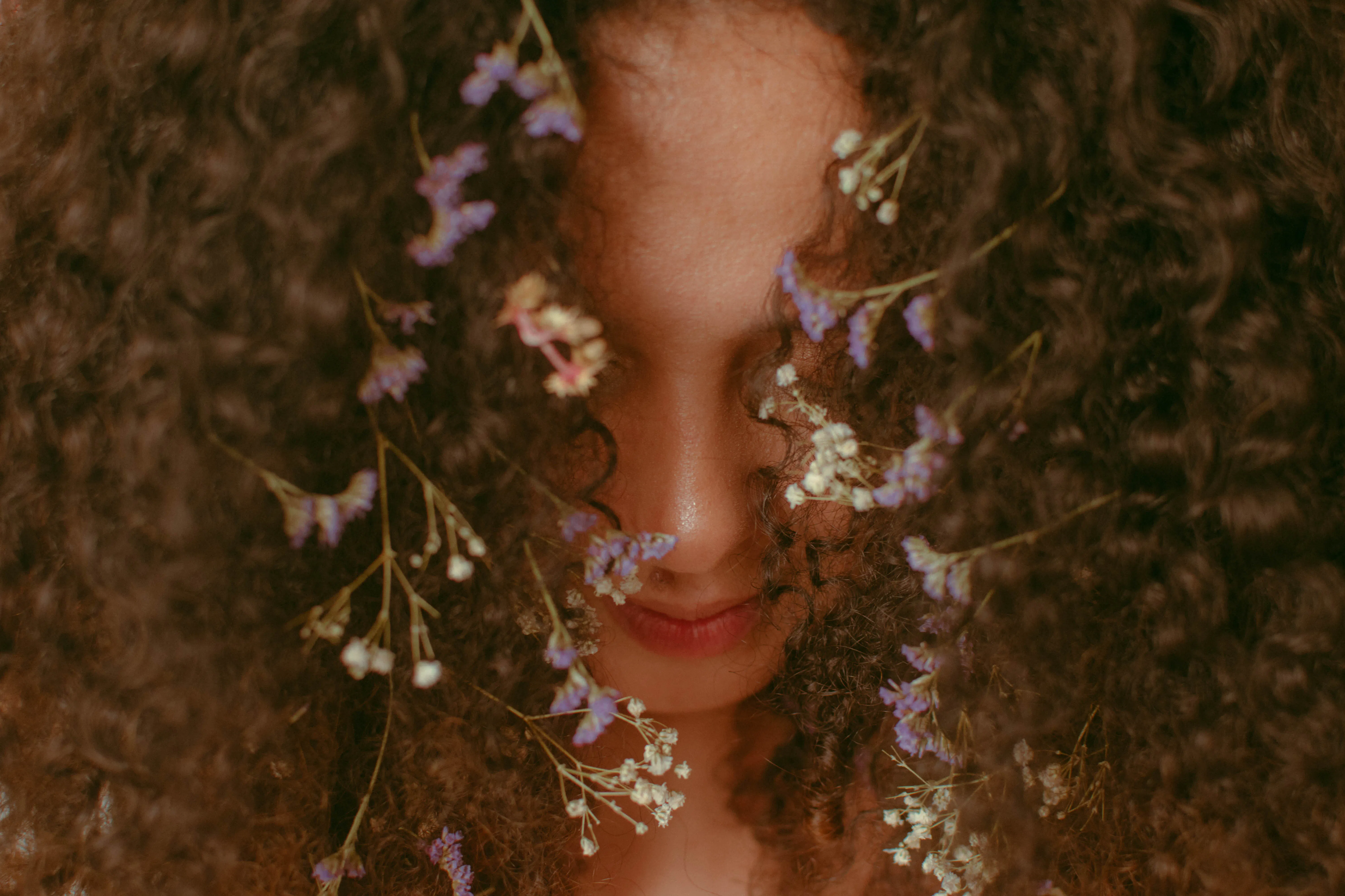 Artistic portrait of a person with curly hair adorned with delicate flowers, symbolizing the natural and creative aspect of AI blog writing when using an AI blog generator.