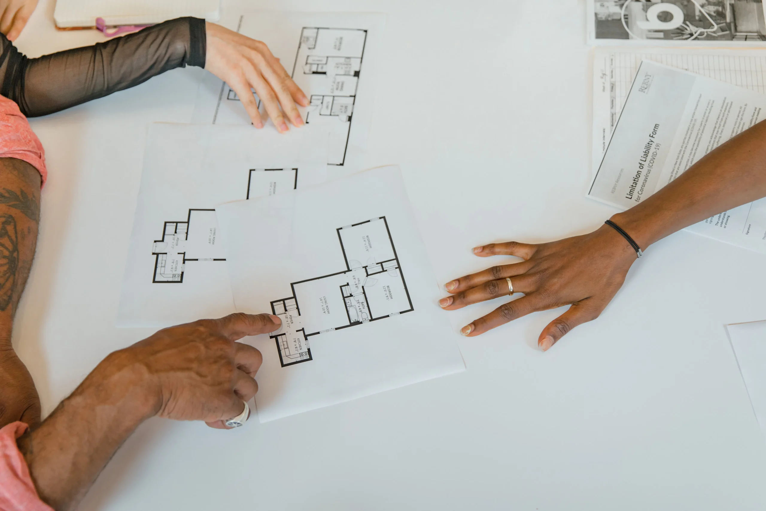 Overhead view of three people reviewing architectural blueprints on a white table.