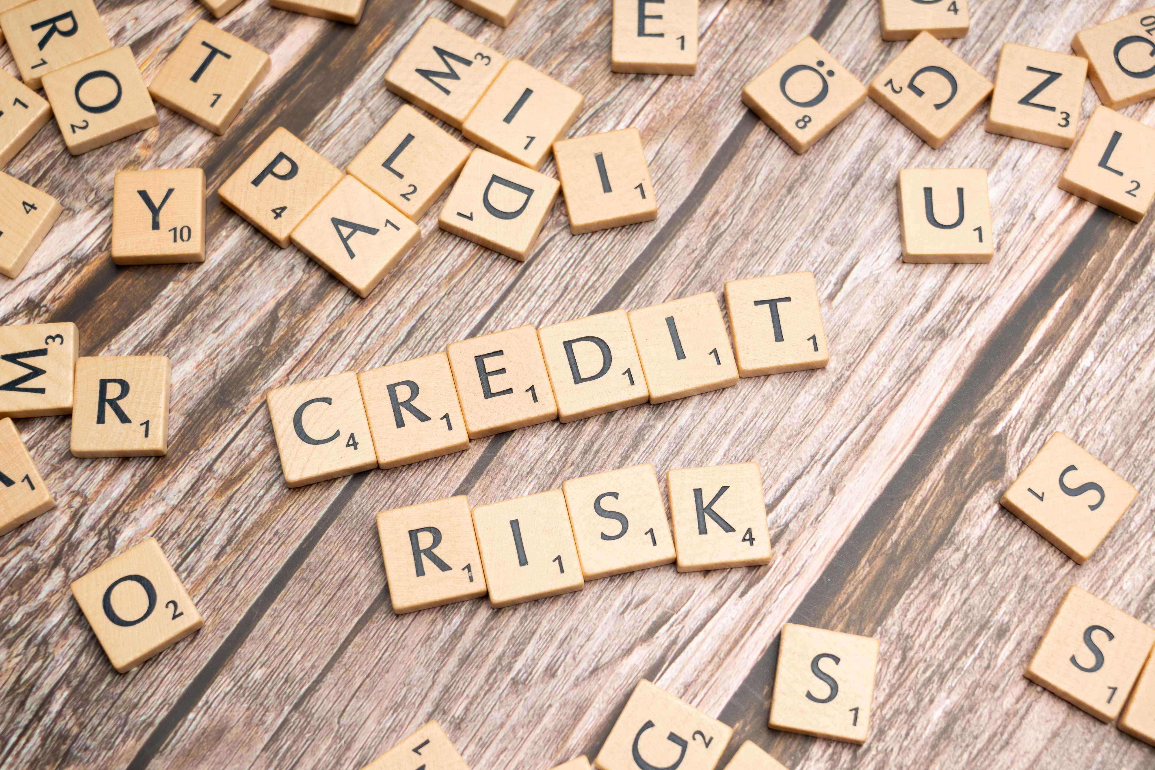 Scrabble tiles spelling 'credit risk' on a wood surface with scattered letters.