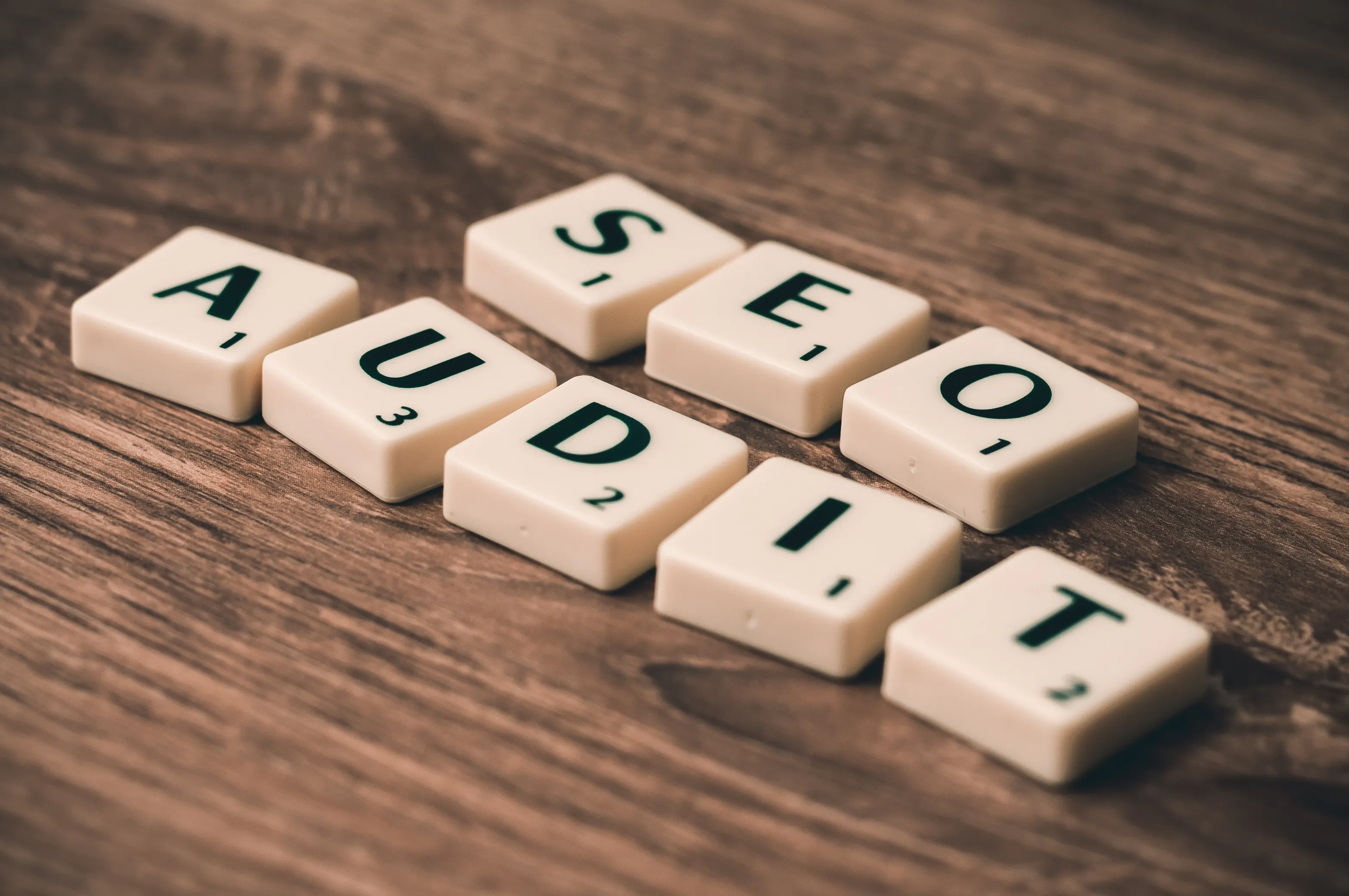 Scrabble tiles spelling out SEO AUDIT on a wood surface.