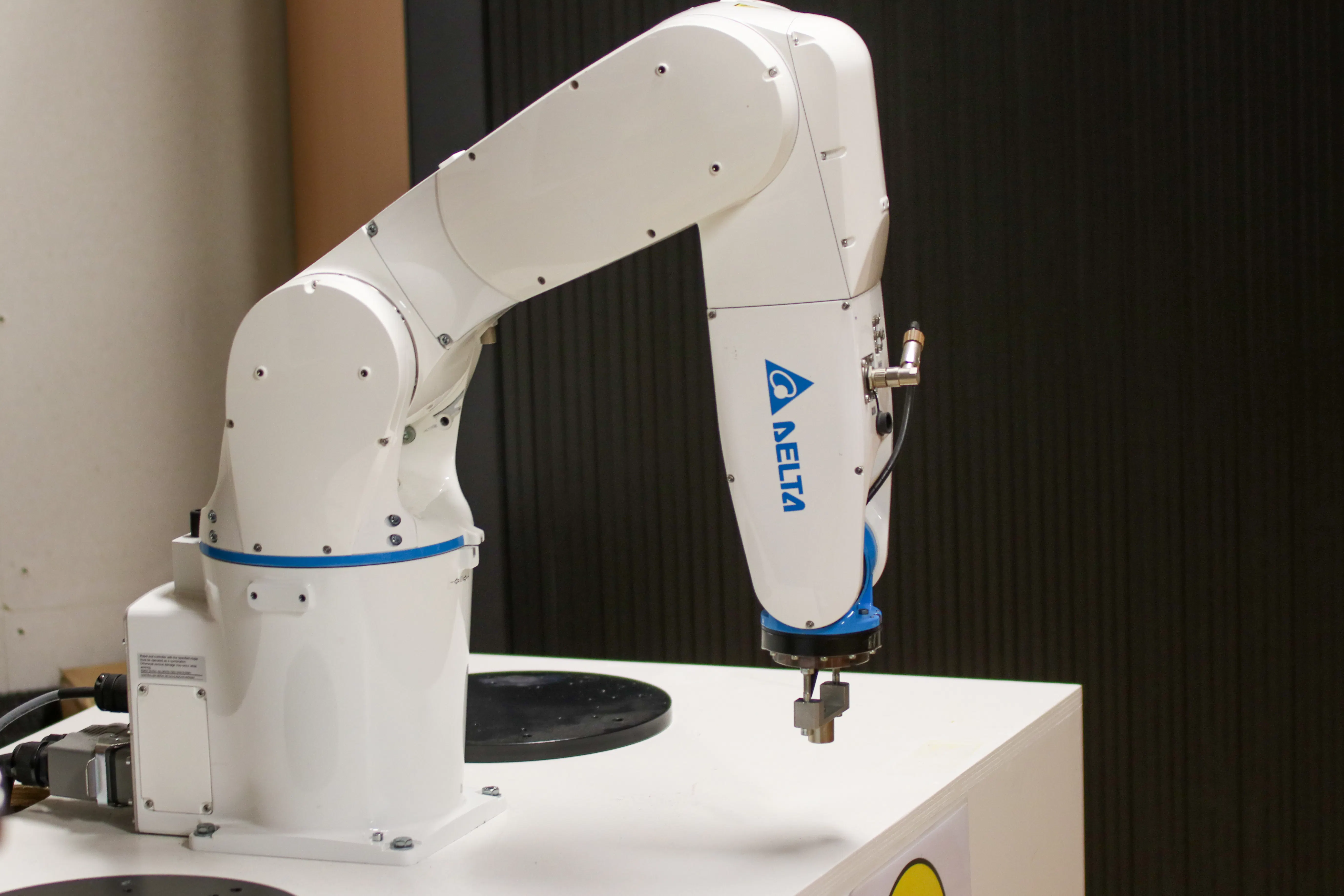 White Delta industrial robotic arm on a white table against a dark wall.