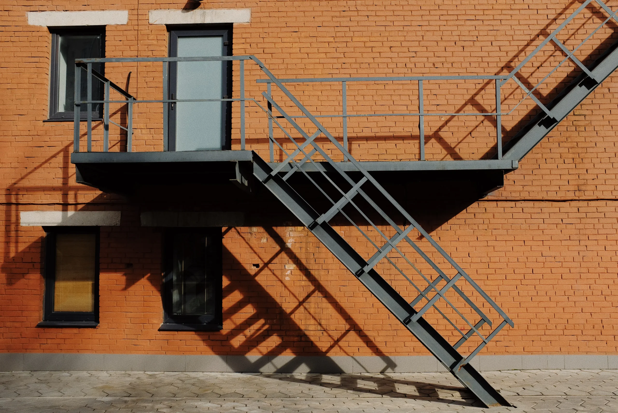 Orange brick building with metal fire escape staircase and small windows.