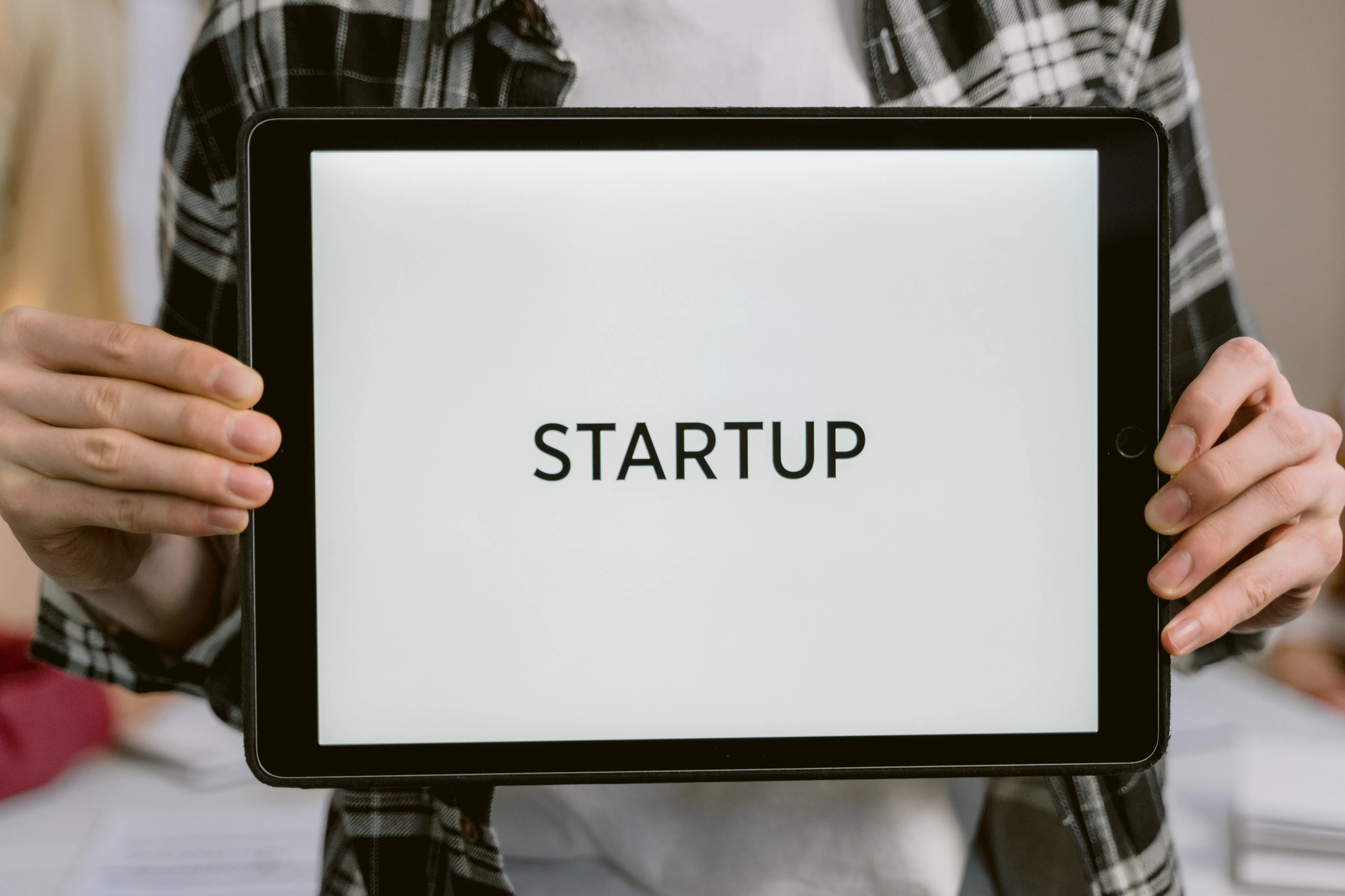 Hands holding tablet displaying the word STARTUP, potentially using AI SEO tools.