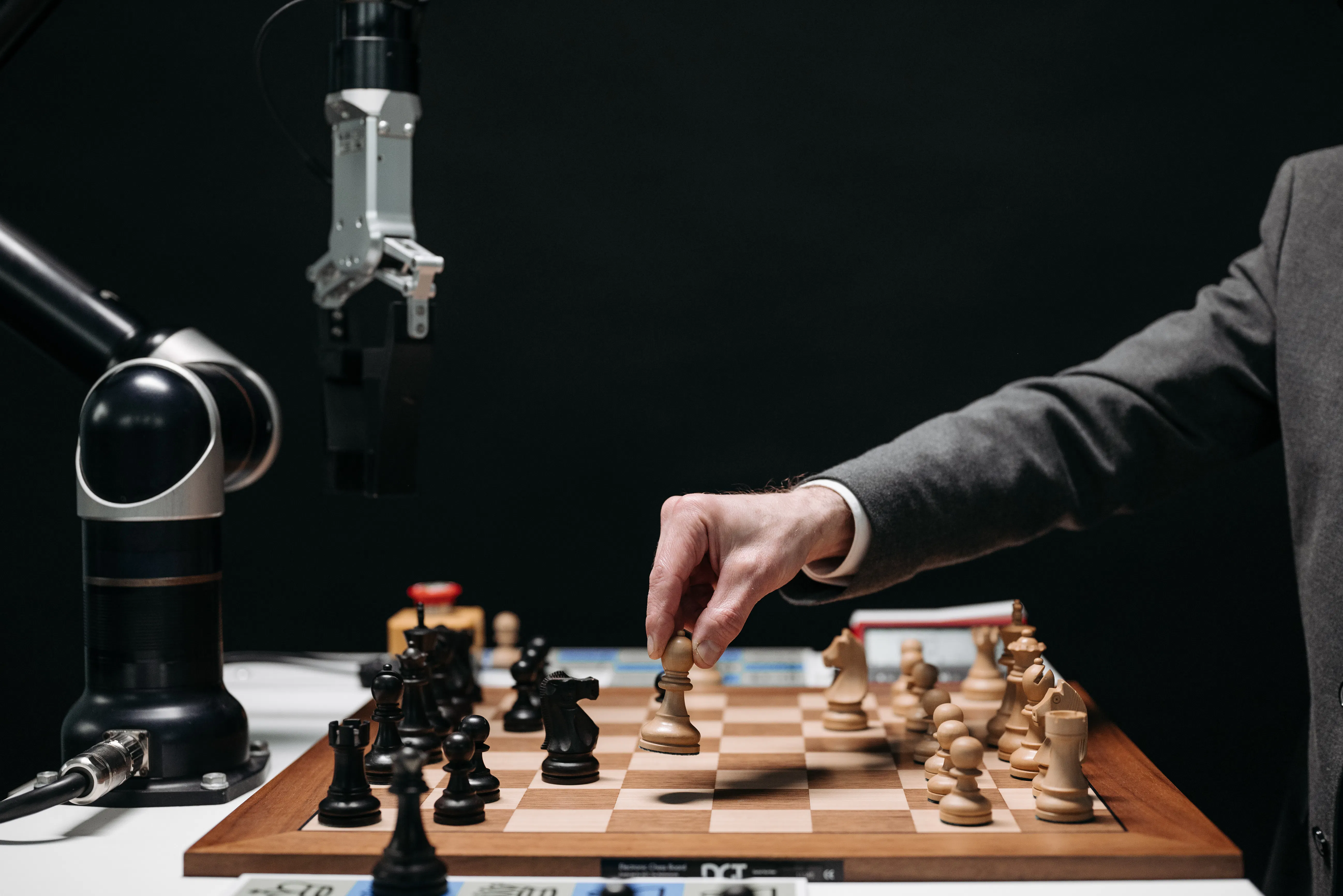 Human hand moving chess piece against robot arm, representing AI vs manual strategy.