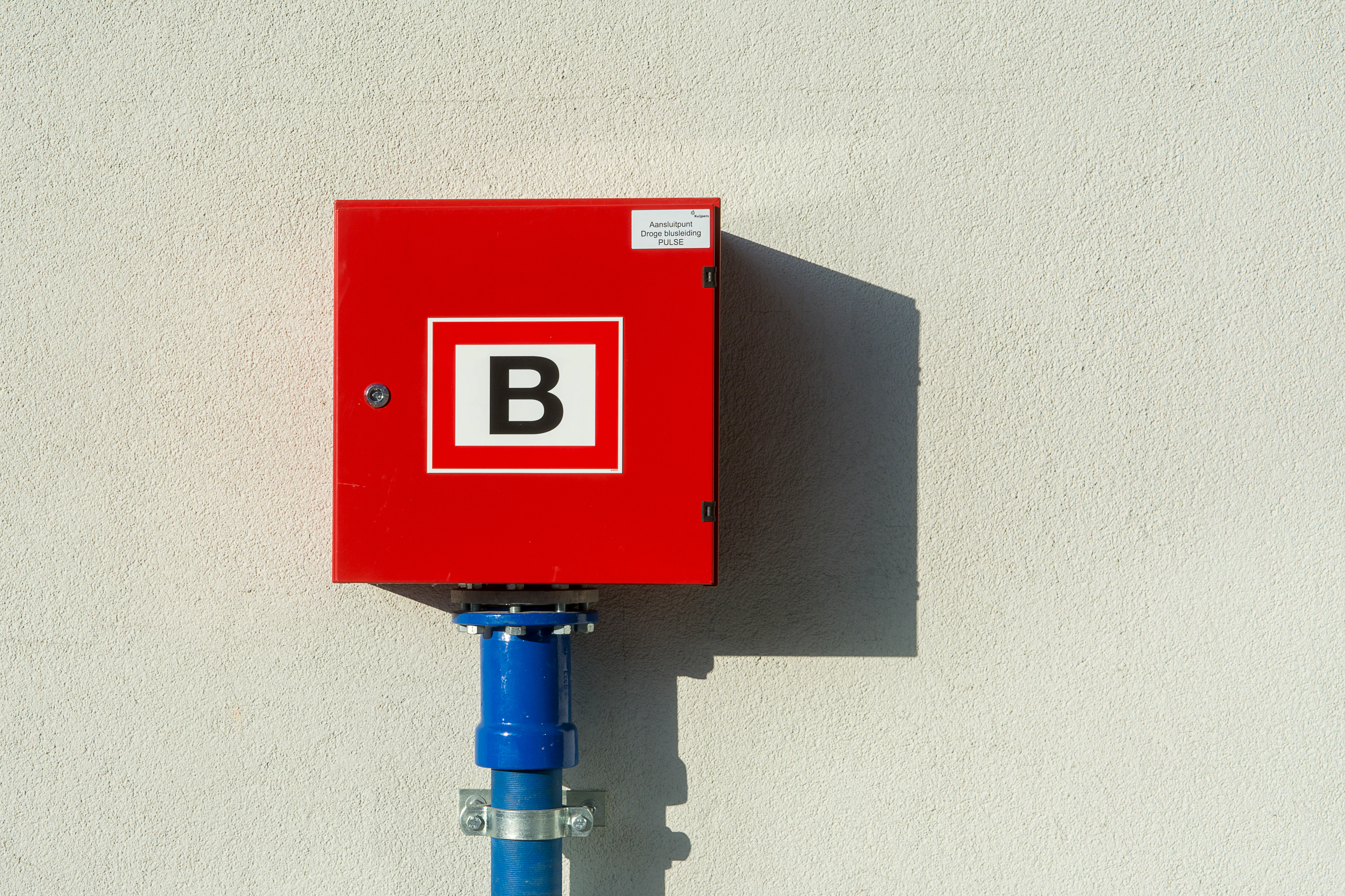 Red square box with white letter B mounted on a light textured wall.