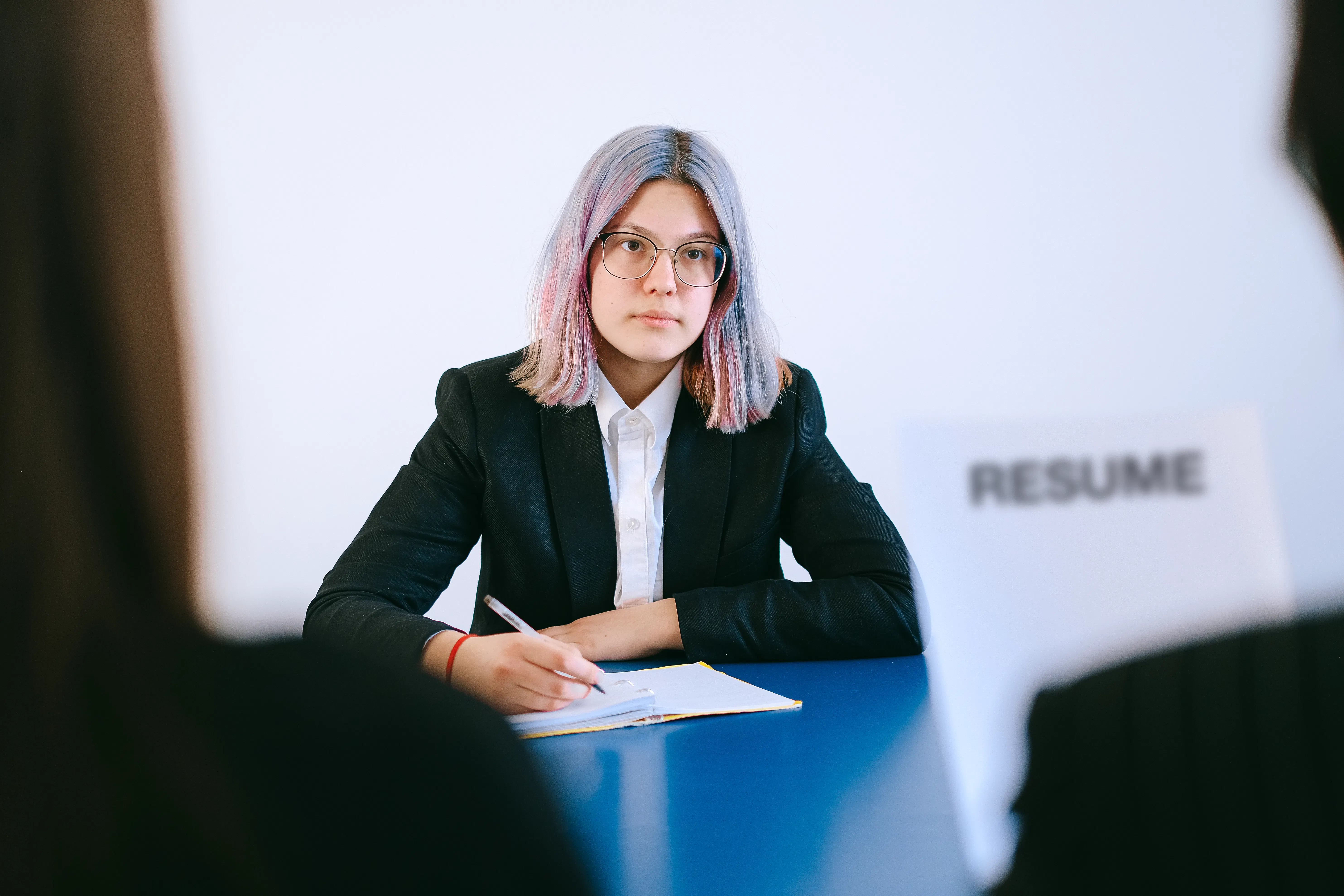 Young woman with colorful hair at a table reviewing a resume, writing on paper.