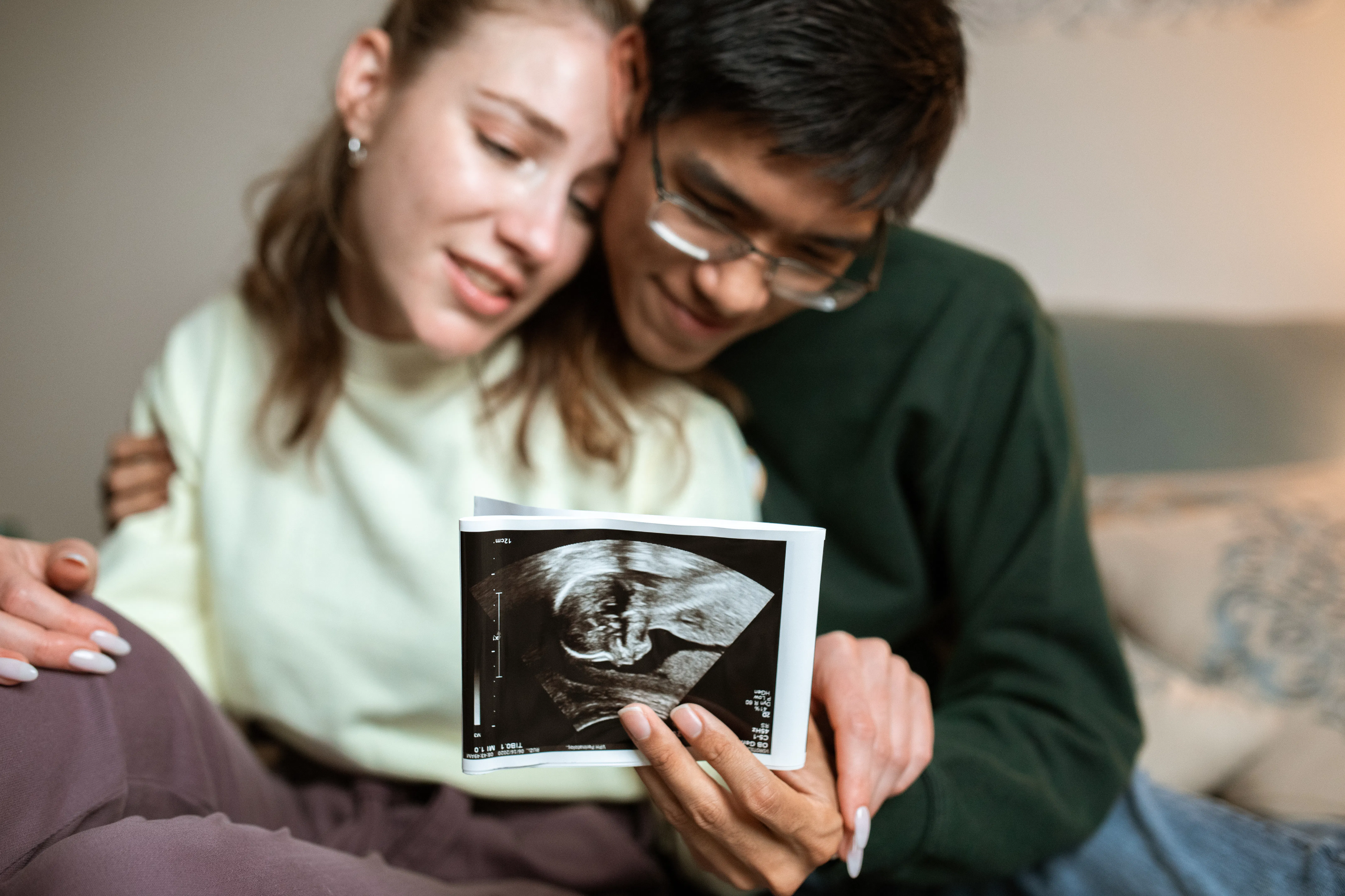 Couple holding ultrasound image, embracing with happy expressions