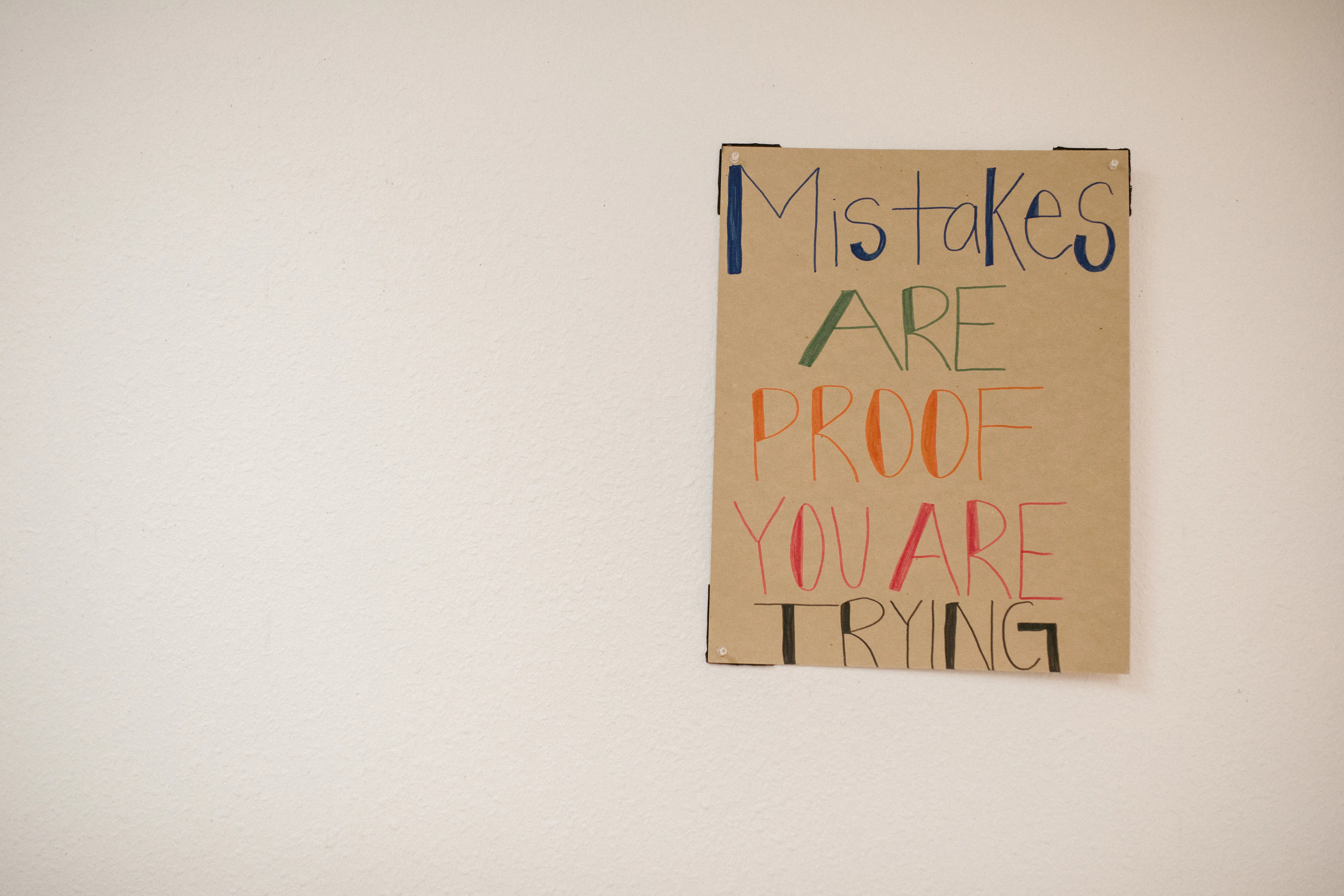 Handmade sign on a white wall reading: 'Mistakes are proof you are trying' in colorful letters.