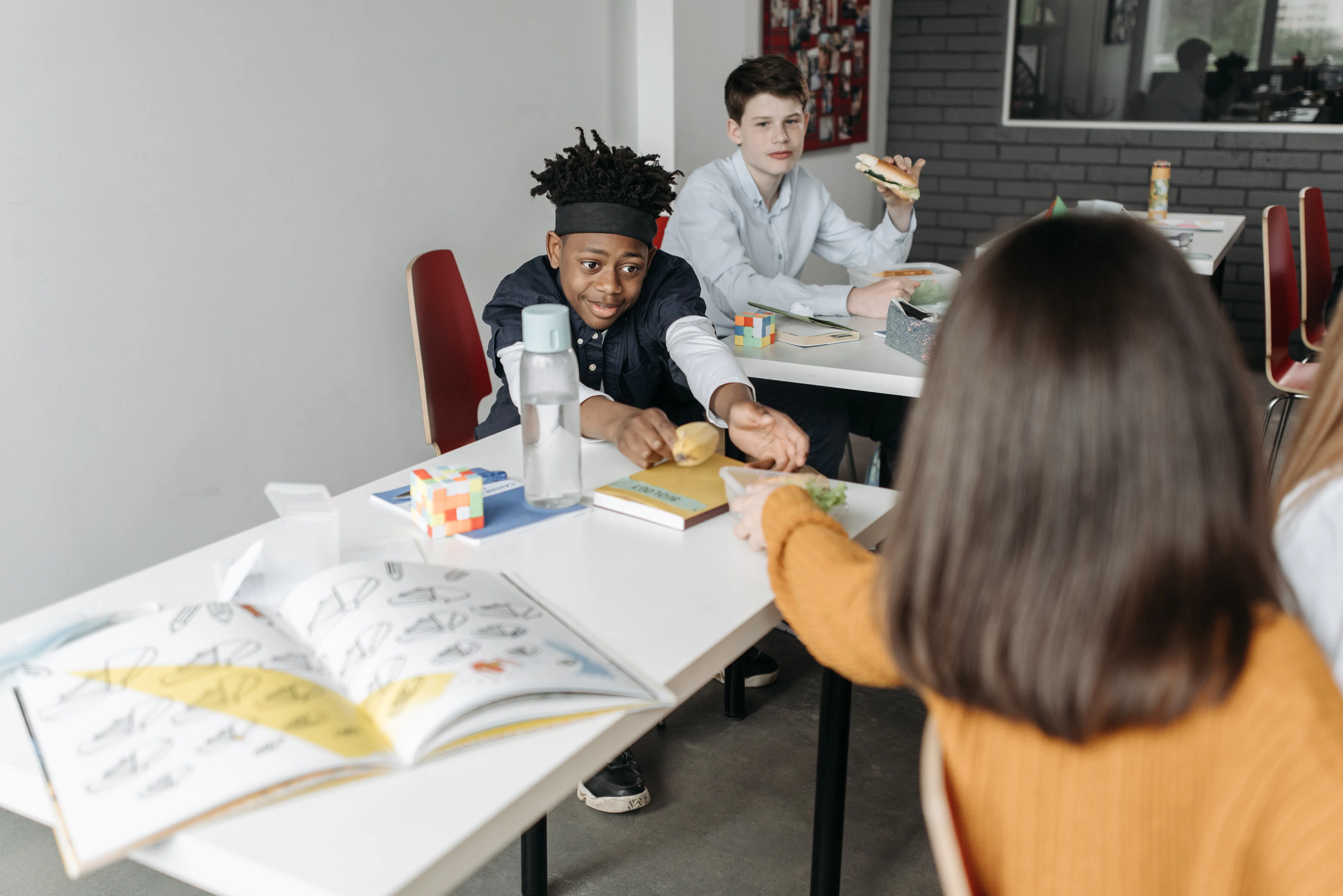 Teenager reaching for food at a table with other students in a classroom.