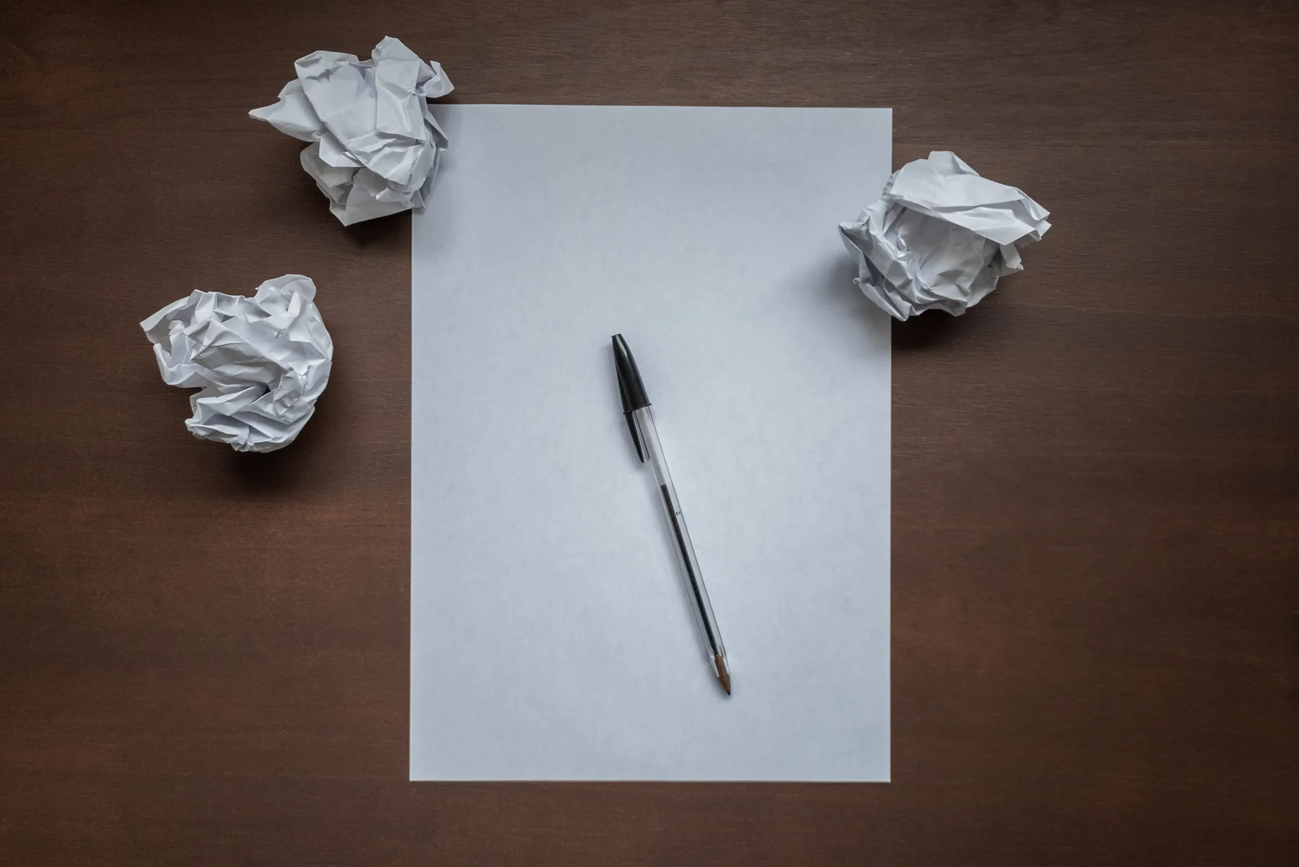 A pen on blank paper with crumpled balls, representing challenges with an automated blog post creator.