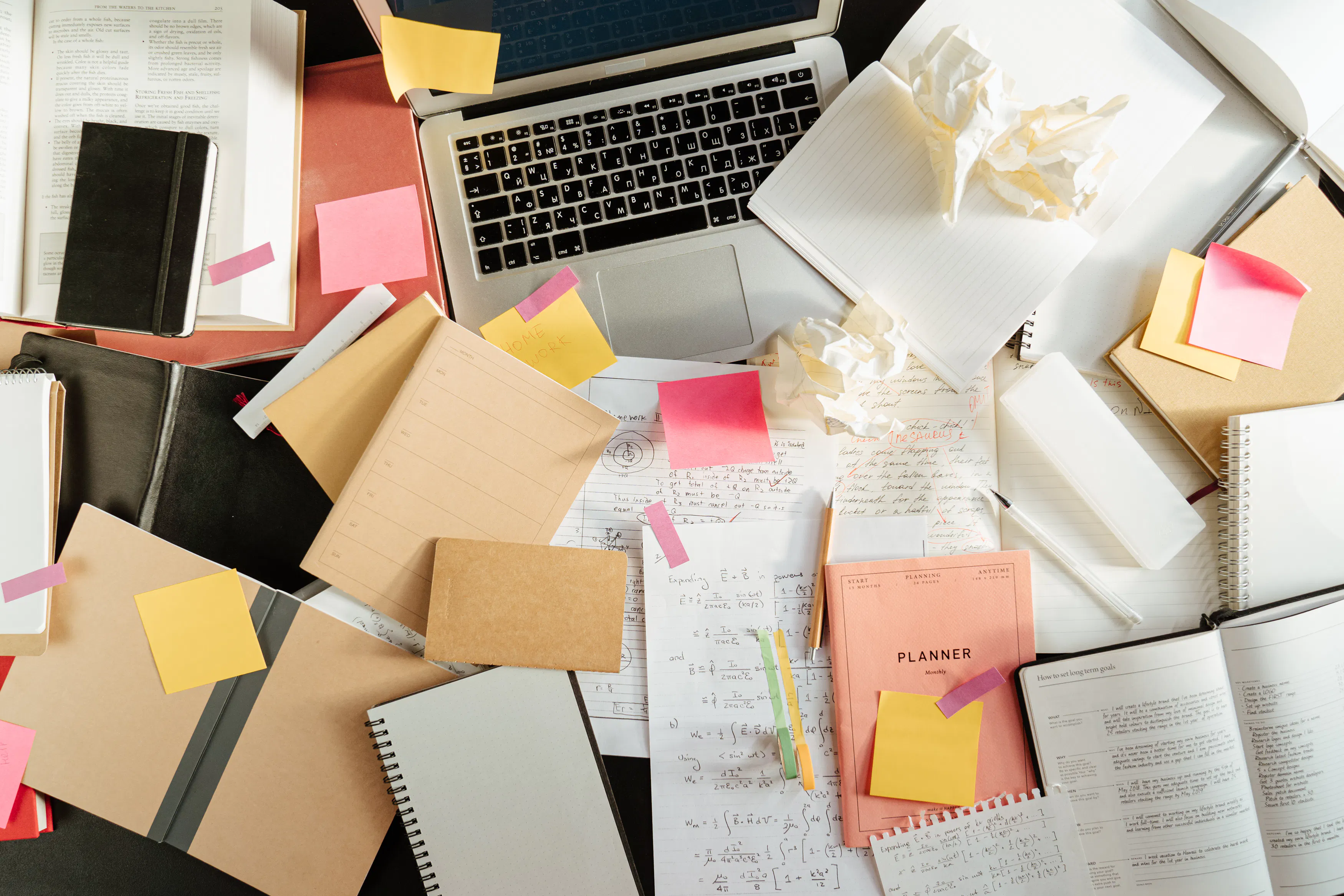 Messy desk with ai copywriting software, notebooks, and papers for editing ai drafts.