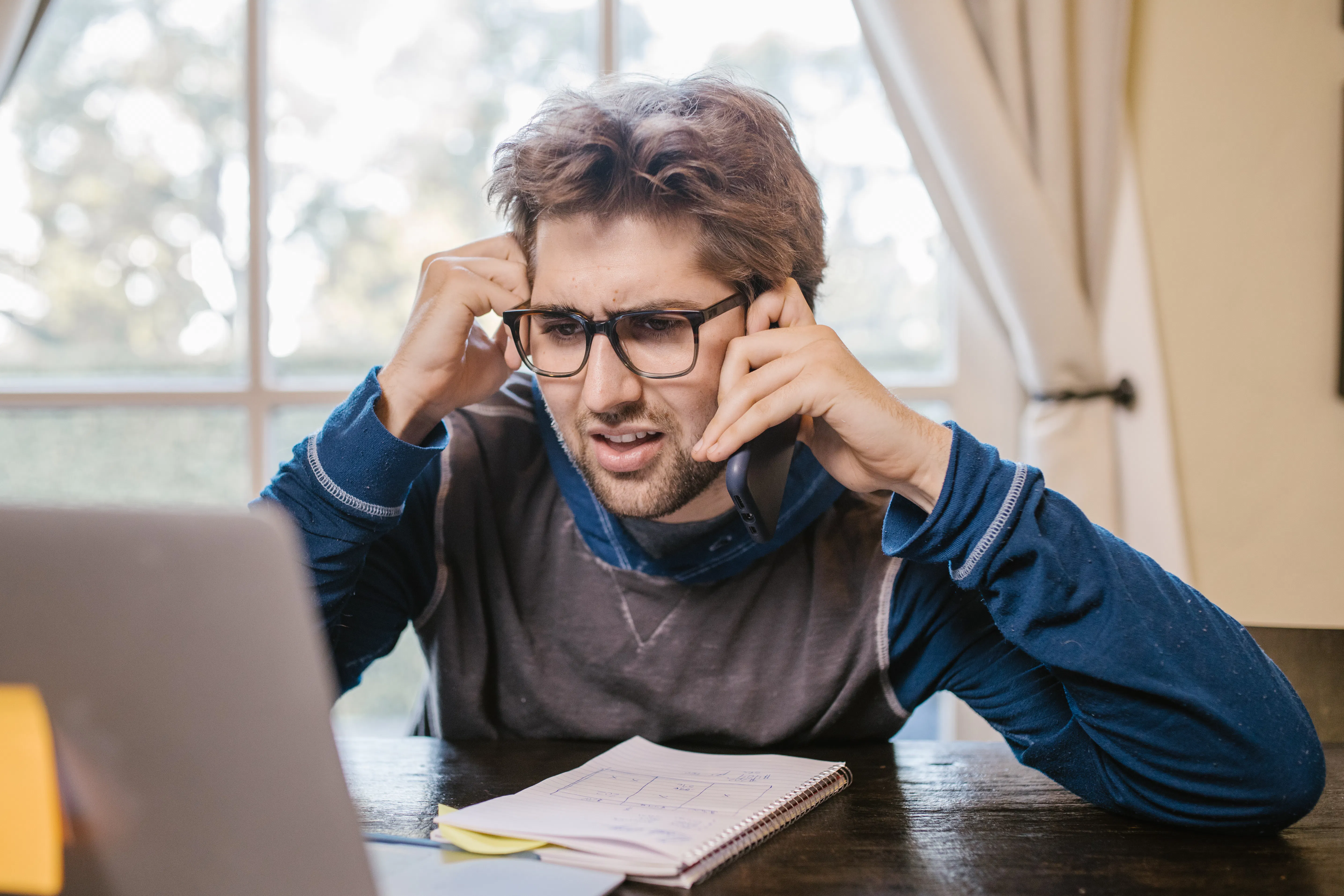 Stressed man on phone looking at laptop, struggling with an ai seo content generator.