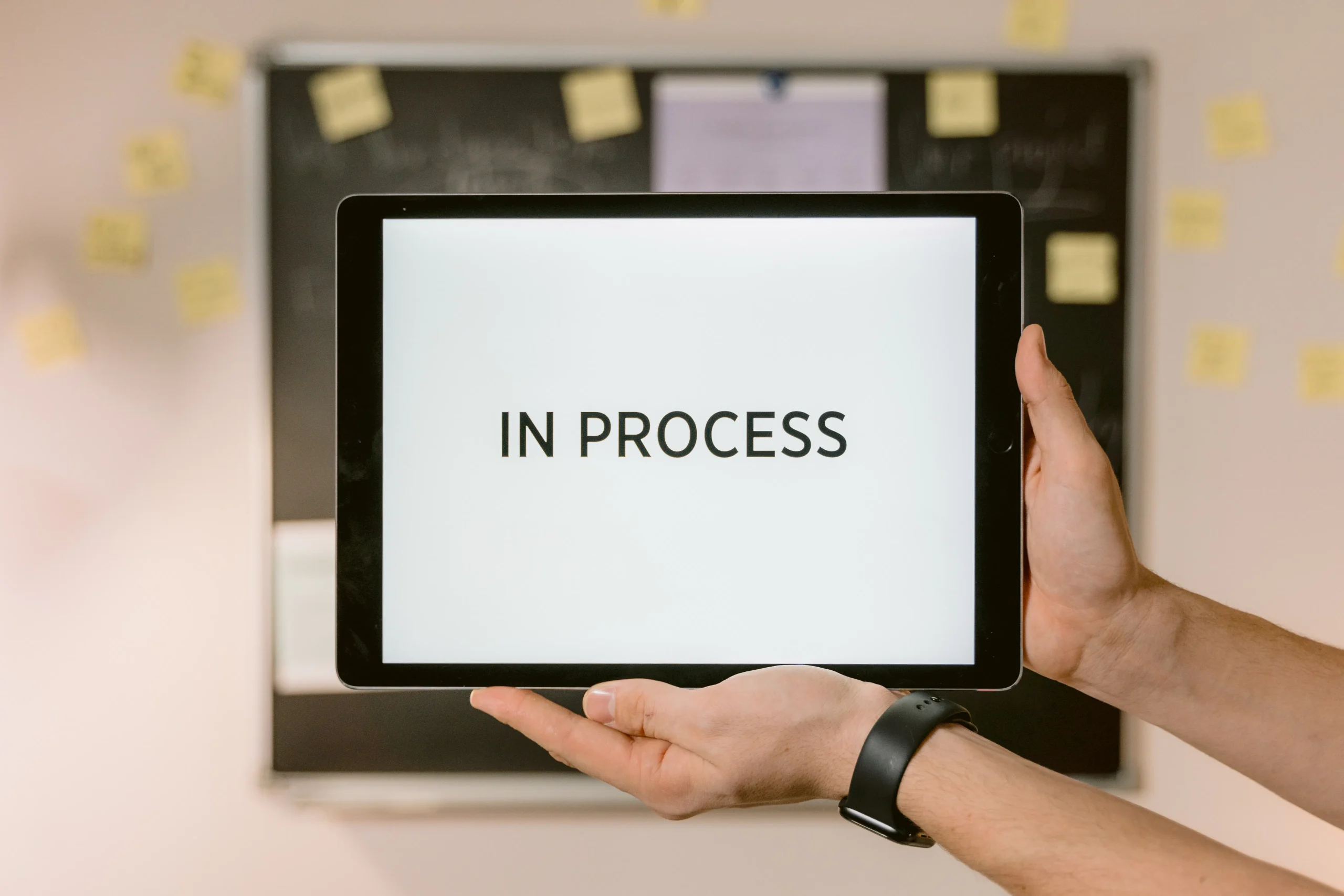 Hands holding a tablet displaying IN PROCESS, representing the evolution of human content creation vs ai writer tools.