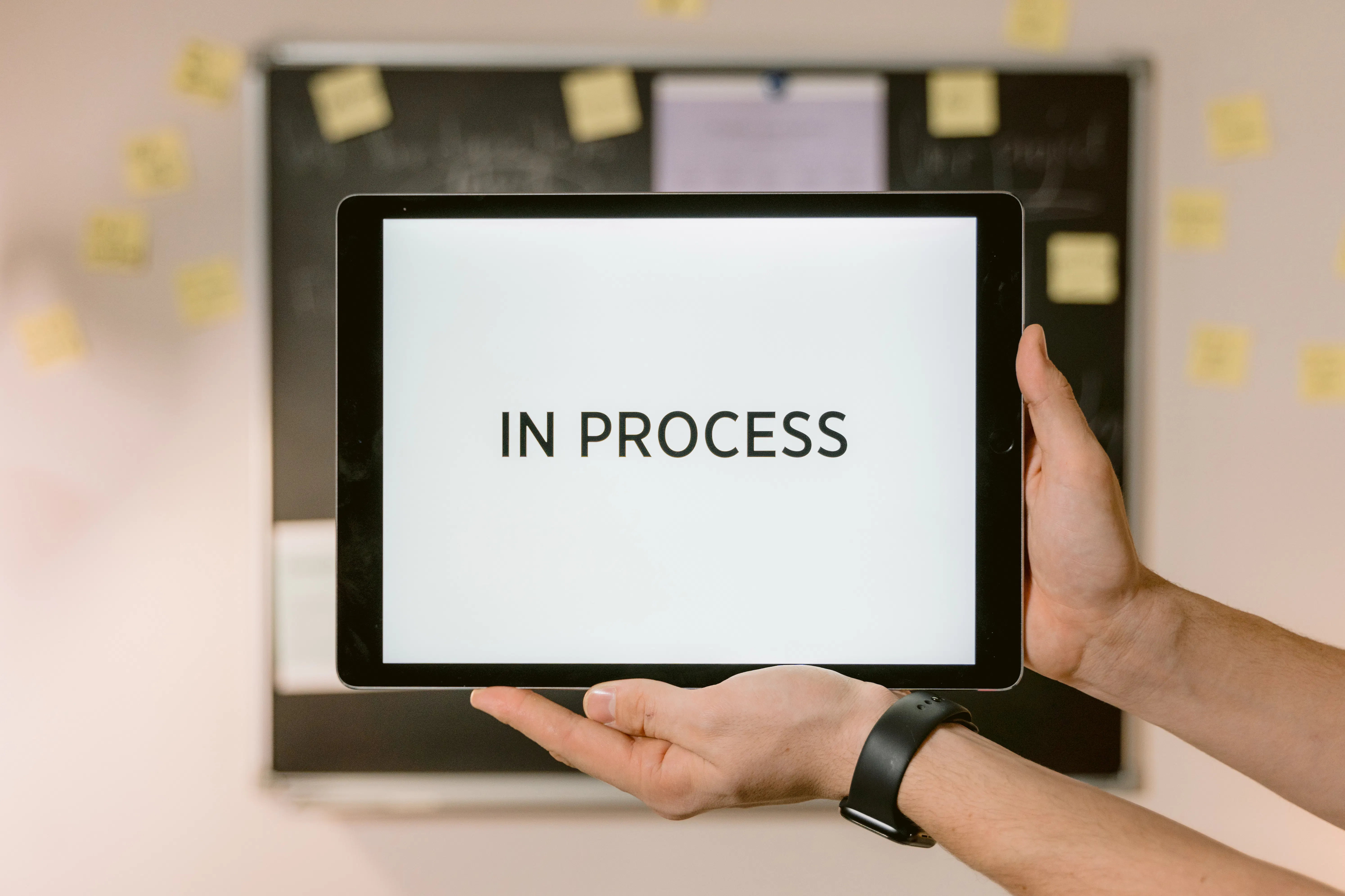 Hands holding a tablet displaying 'IN PROCESS