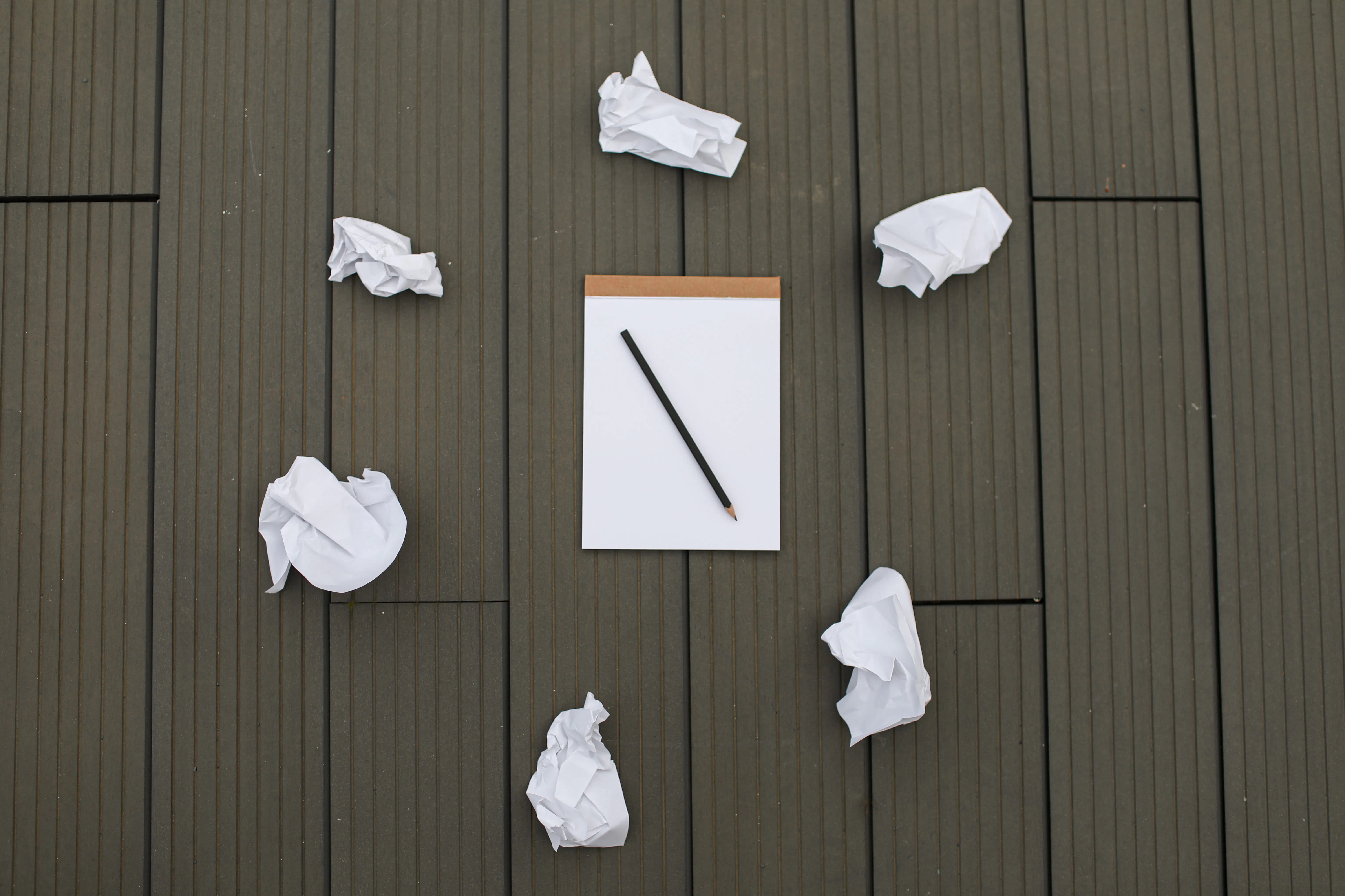 Blank notebook and pencil surrounded by crumpled paper, representing challenges in ai content creation.