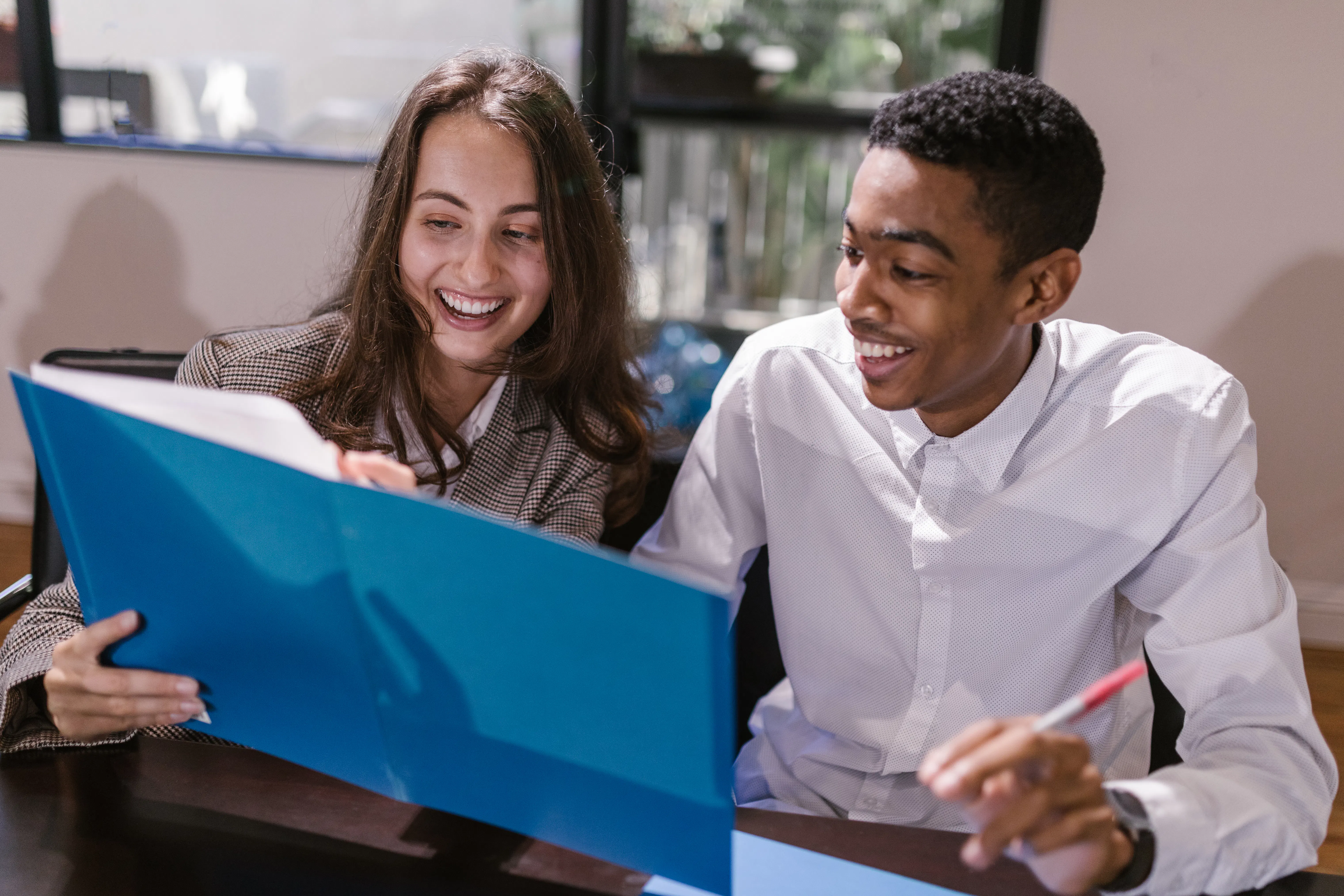 Two colleagues smiling while reviewing marketing automation tools in a blue folder.