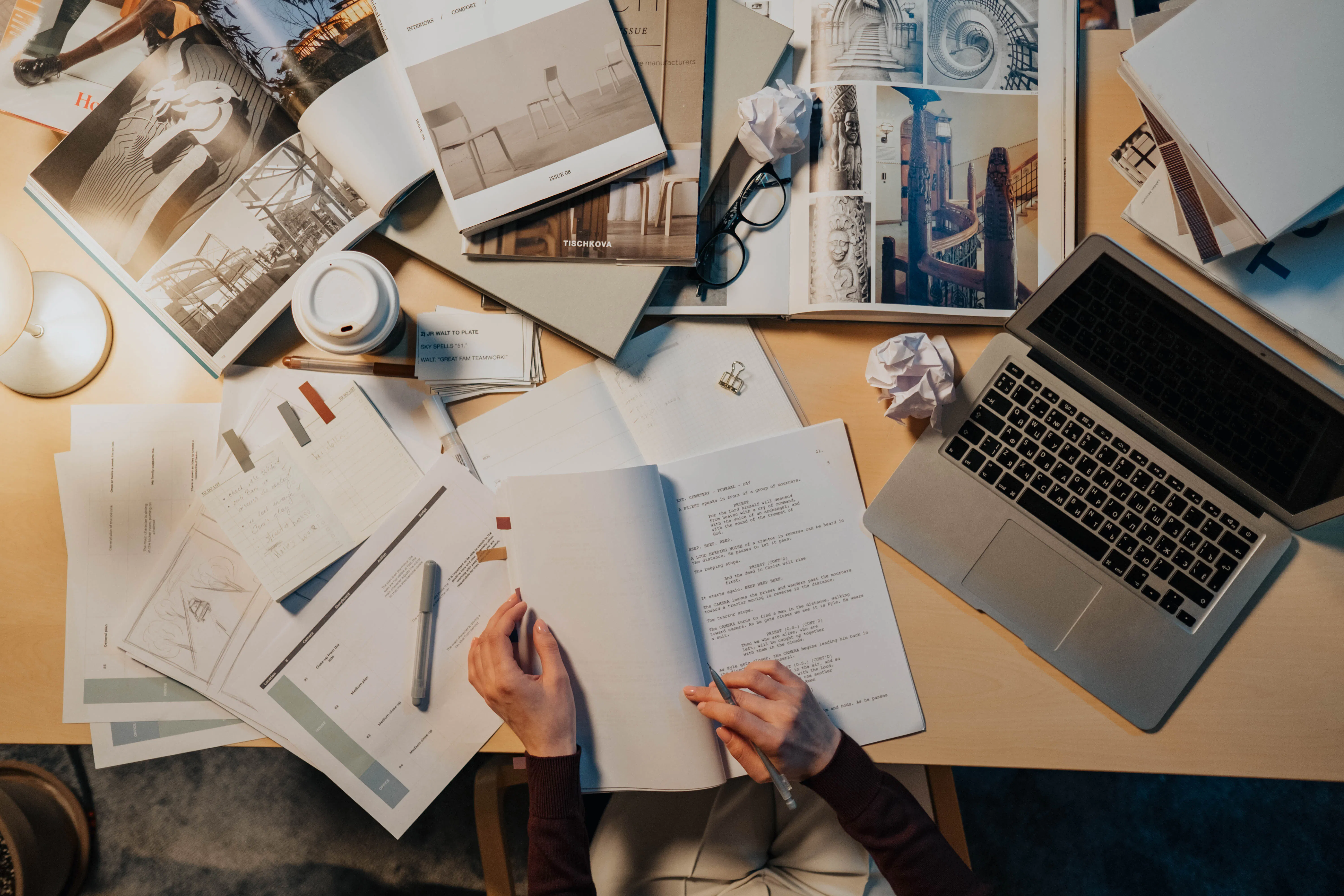 A person writing at a cluttered desk with a laptop, comparing paid vs free ai writers for content creation.