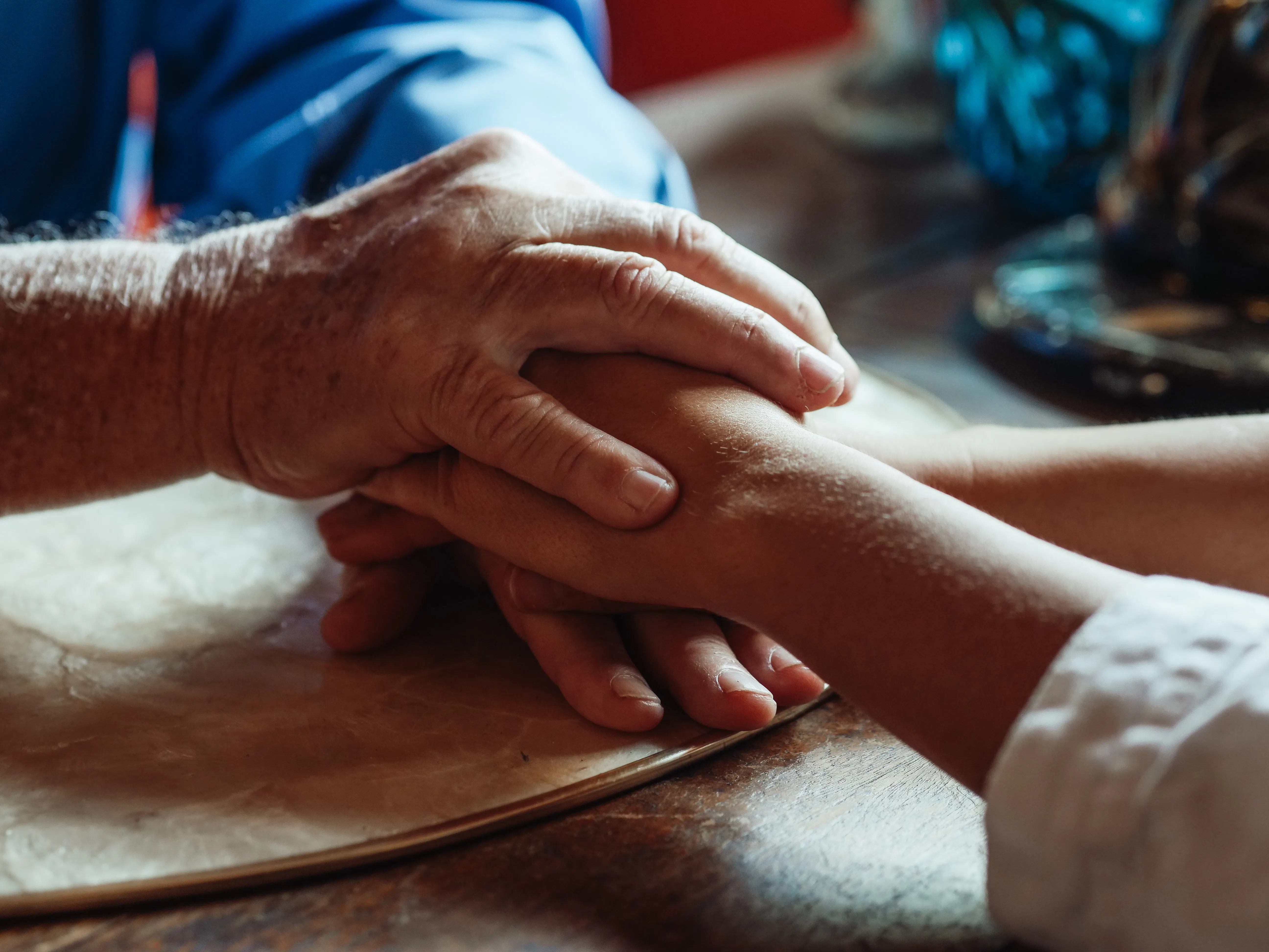 Older, wrinkled hands gently holding a younger person's hand, symbolizing human connection and empathy that AI copywriting software lacks.